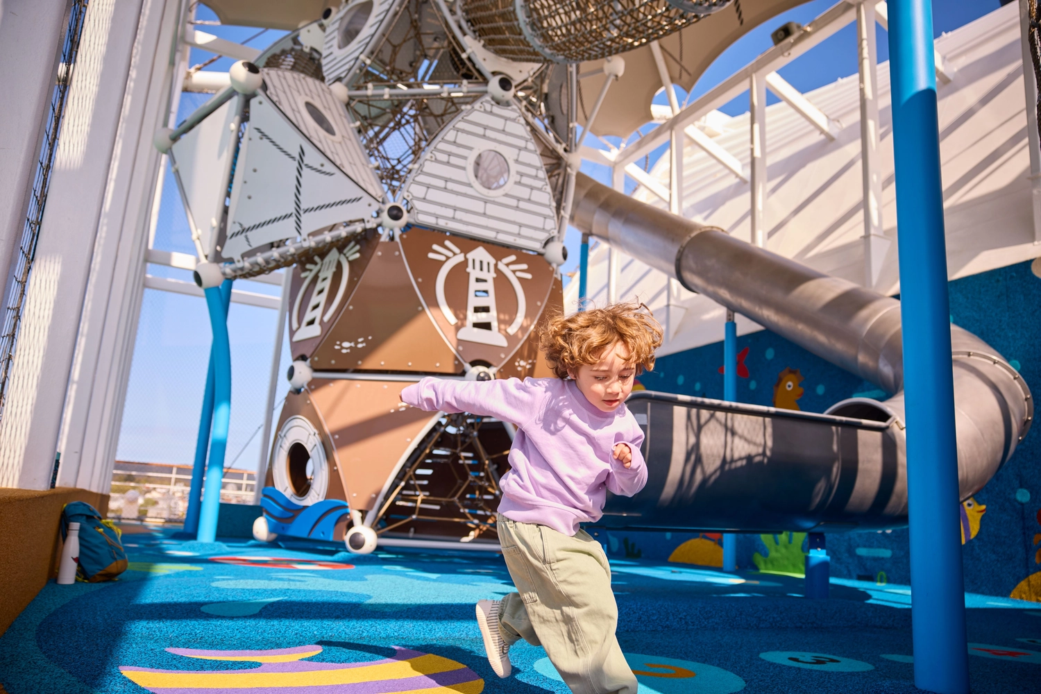 GTS - Reiseservice - Ein kleines Kind tobt auf dem Spielplatz eines Kreuzfahrtschiffs mit einem großen Klettergerüst und einer Metallrutsche.
