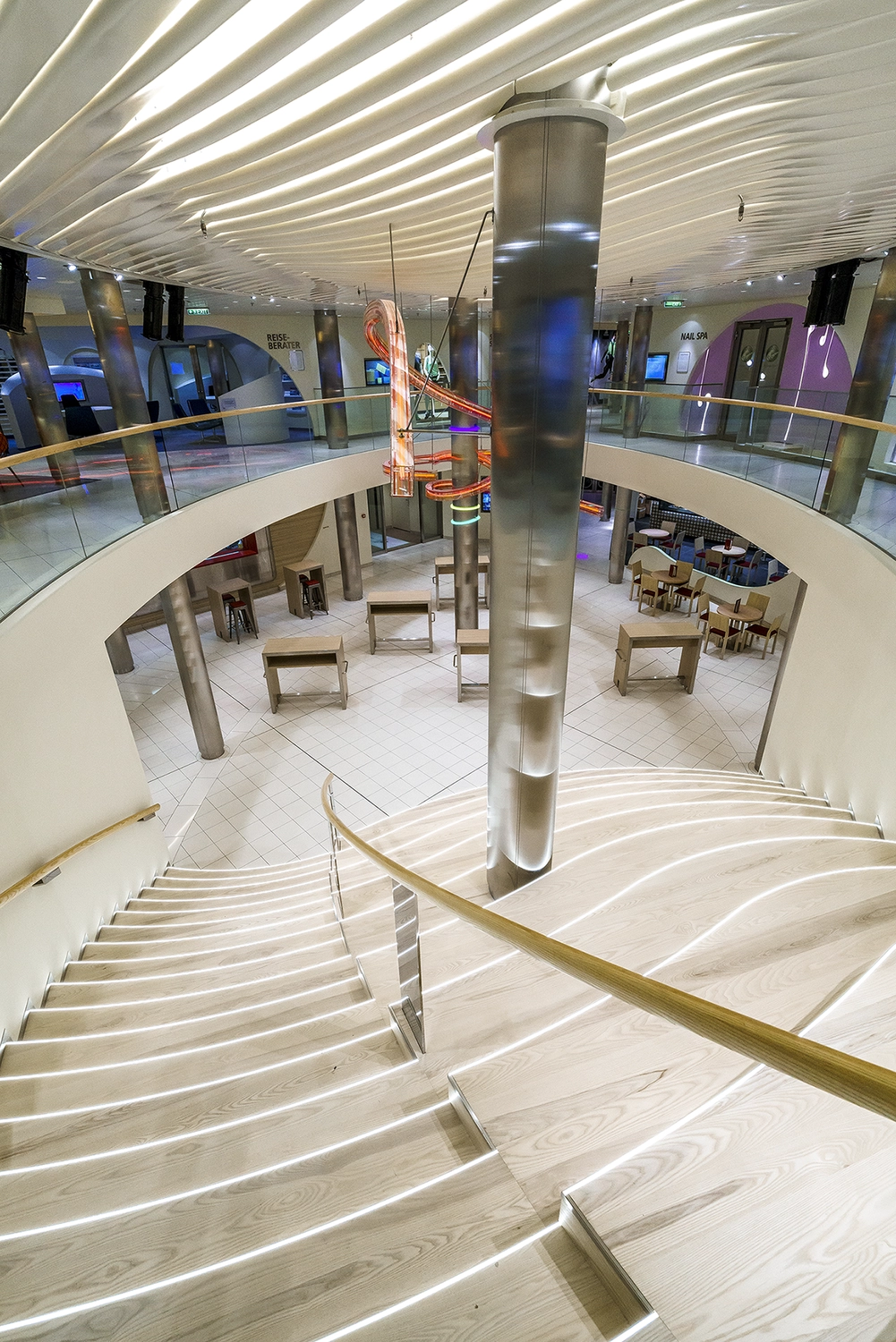 GTS - Reiseservice - Modernes Atrium eines Kreuzfahrtschiffs mit einer breiten, beleuchteten Treppe, die zu einem zentralen Loungebereich hinunterführt.