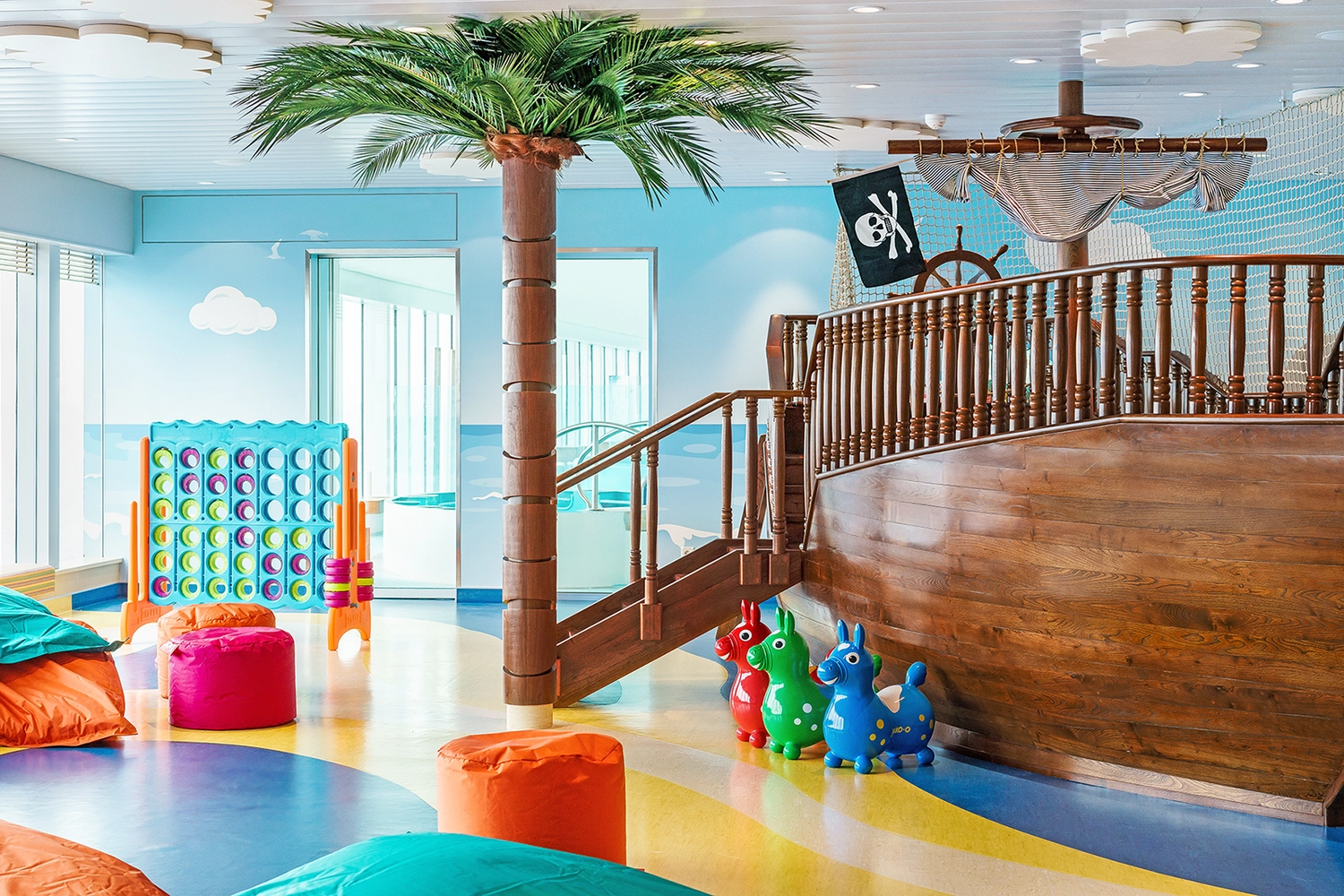 GTS – Reiseservice – Ein Indoor-Spielzimmer in Form eines Kreuzfahrtschiffs mit einem großen Piratenschiff aus Holz, einer dekorativen Palme, Sitzsäcken und buntem Spielzeug.