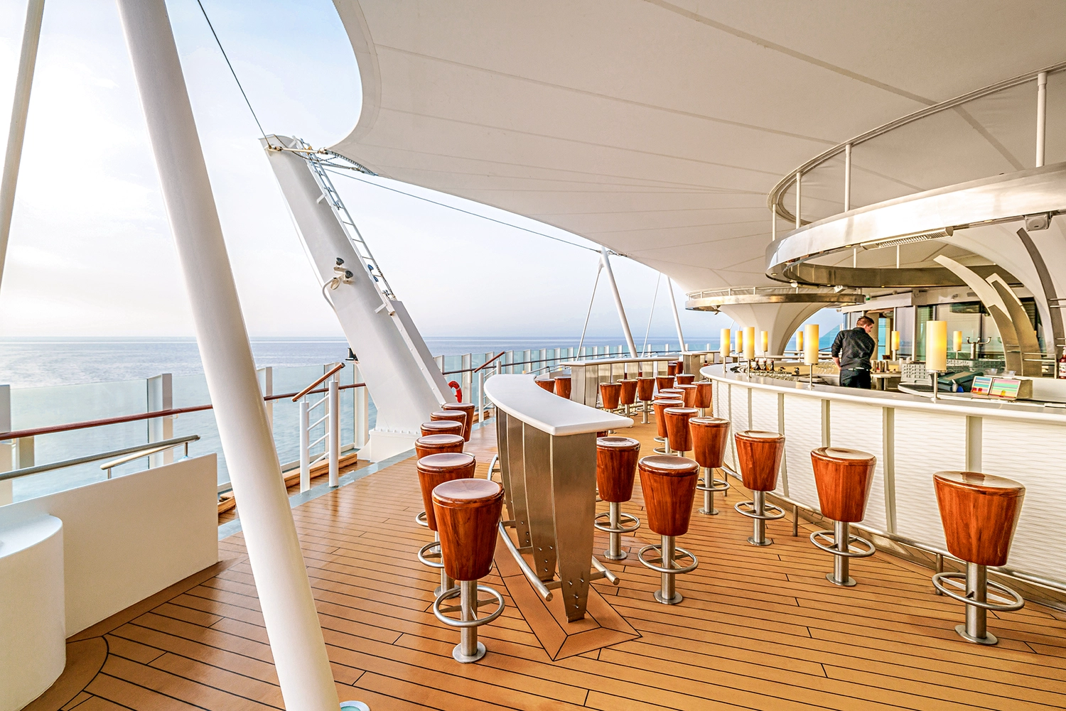 GTS - Reiseservice - Eine Open-Air-Bar auf einem Kreuzfahrtschiff mit Holzhockern unter einem großen weißen Baldachin.
