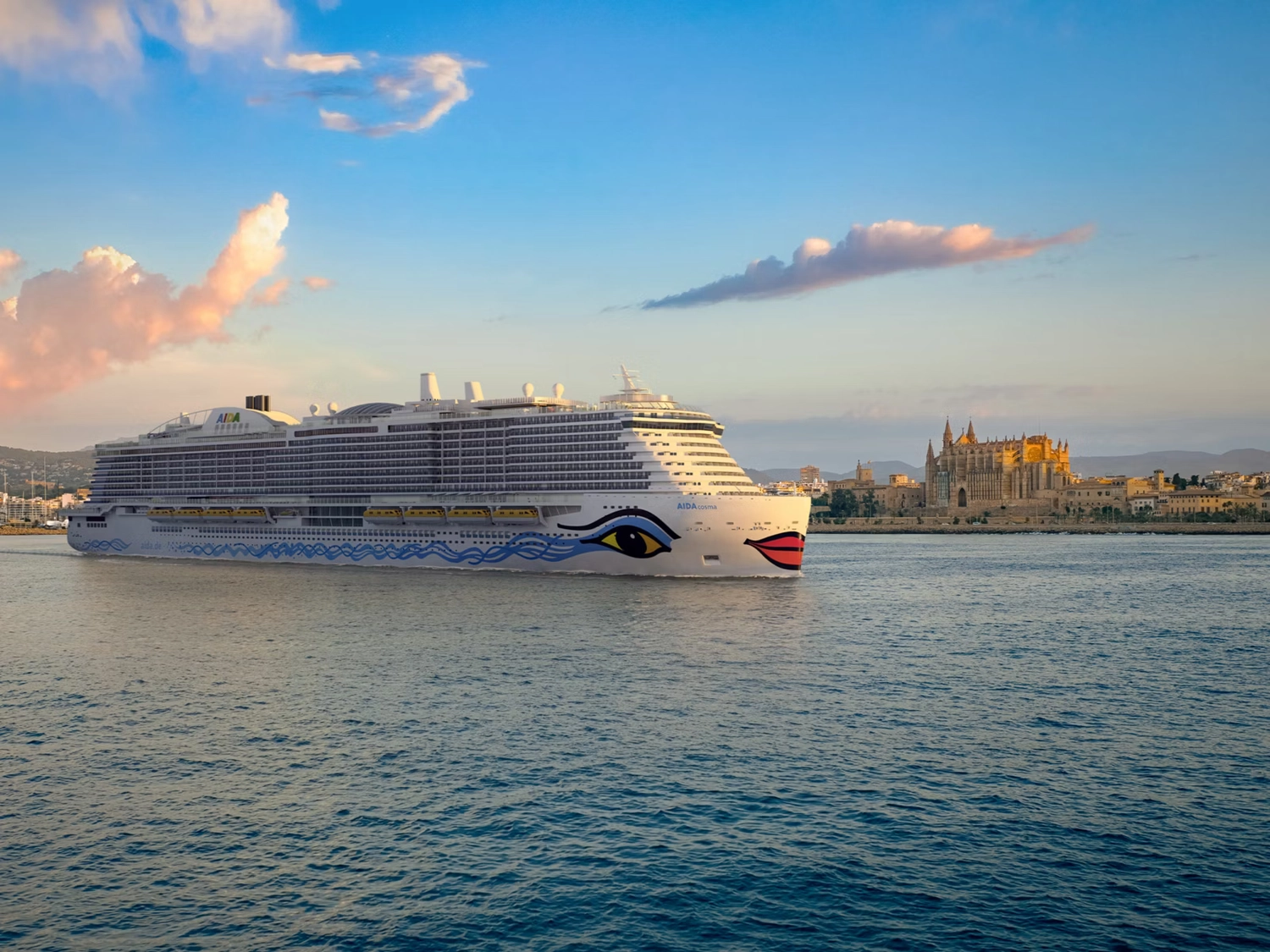 GTS – Reiseservice – Ein Kreuzfahrtschiff mit auffälligen Augen- und Lippenmotiven fährt an einer Kathedrale in einer Küstenstadt vorbei.