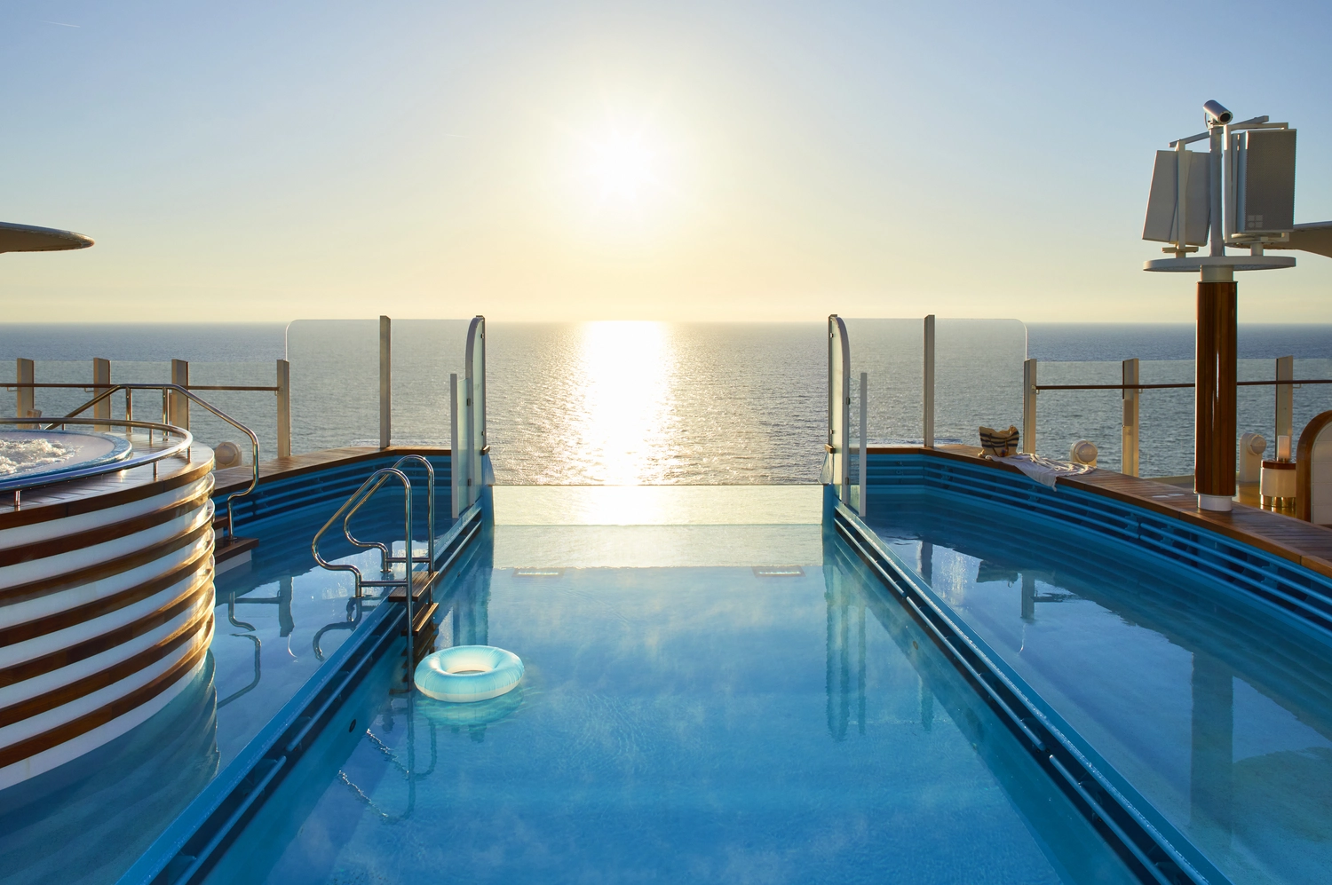 GTS - Reiseservice - Infinity-Pool eines Kreuzfahrtschiffs mit Blick auf den hellen, sonnenbeschienenen Ozean.