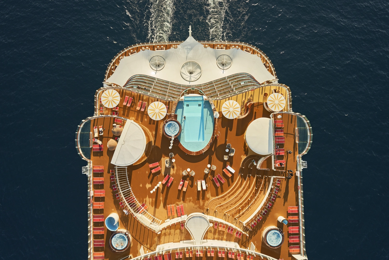 GTS - Reiseservice - Luftaufnahme eines Kreuzfahrtschiffdecks mit Swimmingpools, Whirlpools, Liegestühlen und Sonnenschirmen auf See.