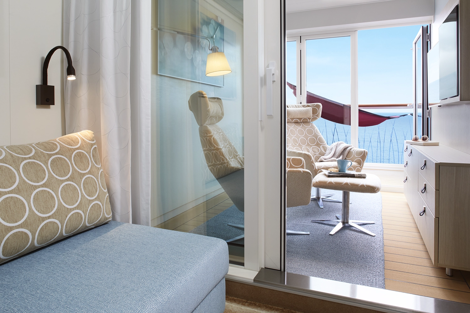 GTS - Reiseservice - Eine moderne Kreuzfahrtkabine mit Zugang zu einem privaten Balkon mit Liegestühlen und Meerblick.
