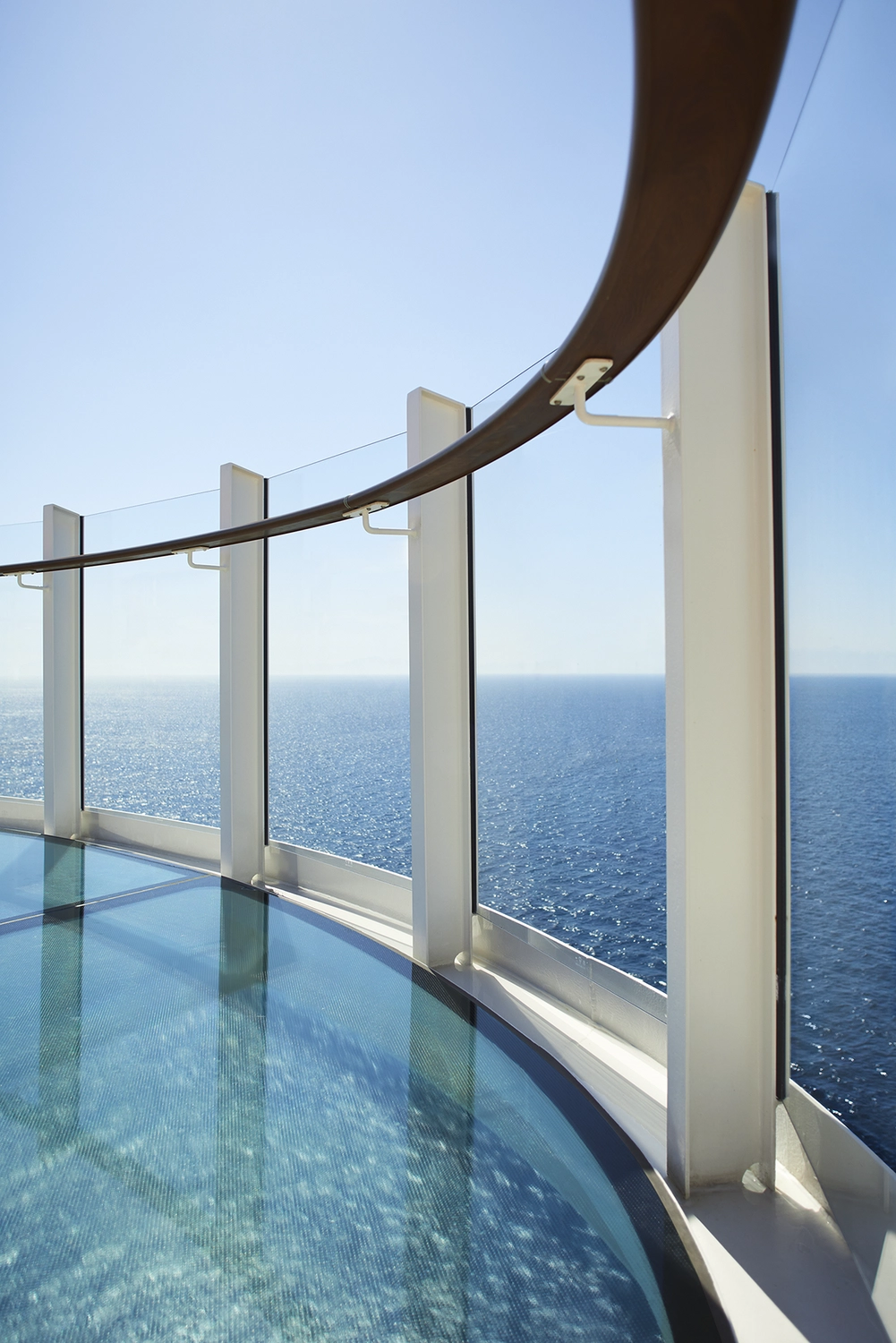 GTS - Reiseservice - Ein geschwungener Glassteg auf einem Kreuzfahrtschiff mit Blick auf das klare, blaue Meer.