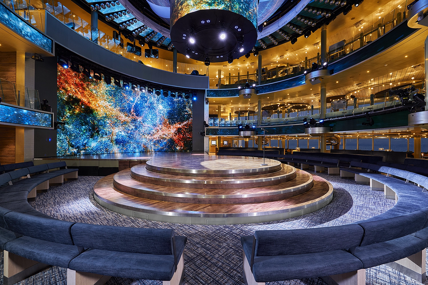 GTS - Reiseservice - Mehrstöckiges Theater auf dem Kreuzfahrtschiff mit einer kreisförmigen, gestuften Bühne und einer riesigen LED-Leinwand, die einen Weltraumnebel zeigt.