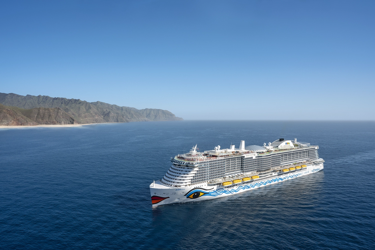 GTS - Reiseservice - Luftaufnahme eines großen weißen Kreuzfahrtschiffs, das durch ruhiges, tiefblaues Wasser fährt.
