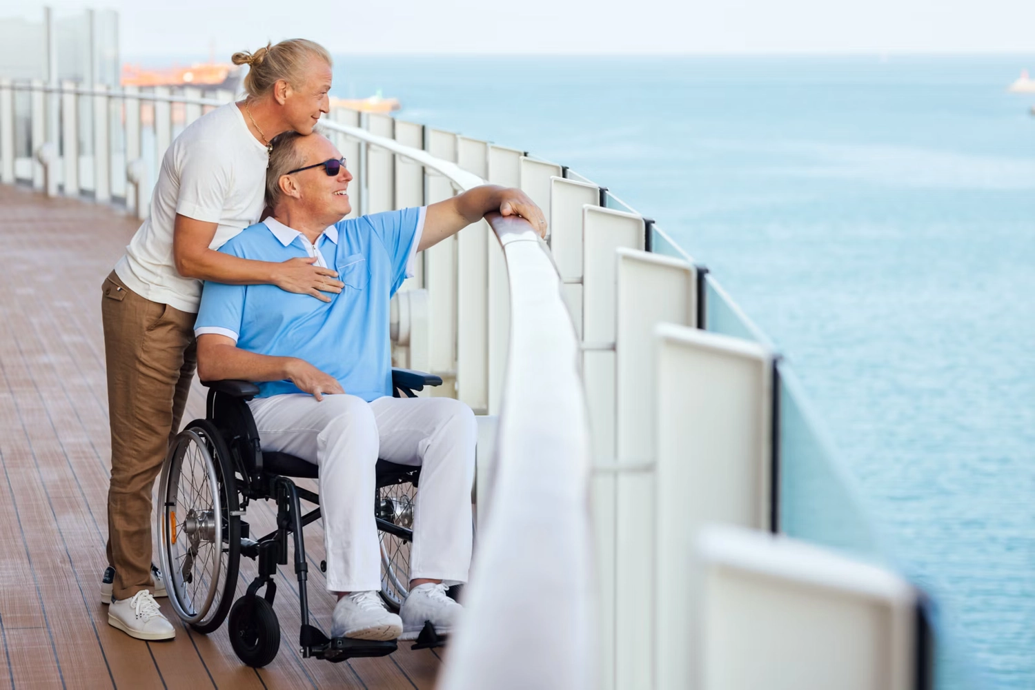 GTS - Reiseservice - Ein älteres Paar an Deck eines Kreuzfahrtschiffs; der Mann im Rollstuhl blickt aufs Meer hinaus.