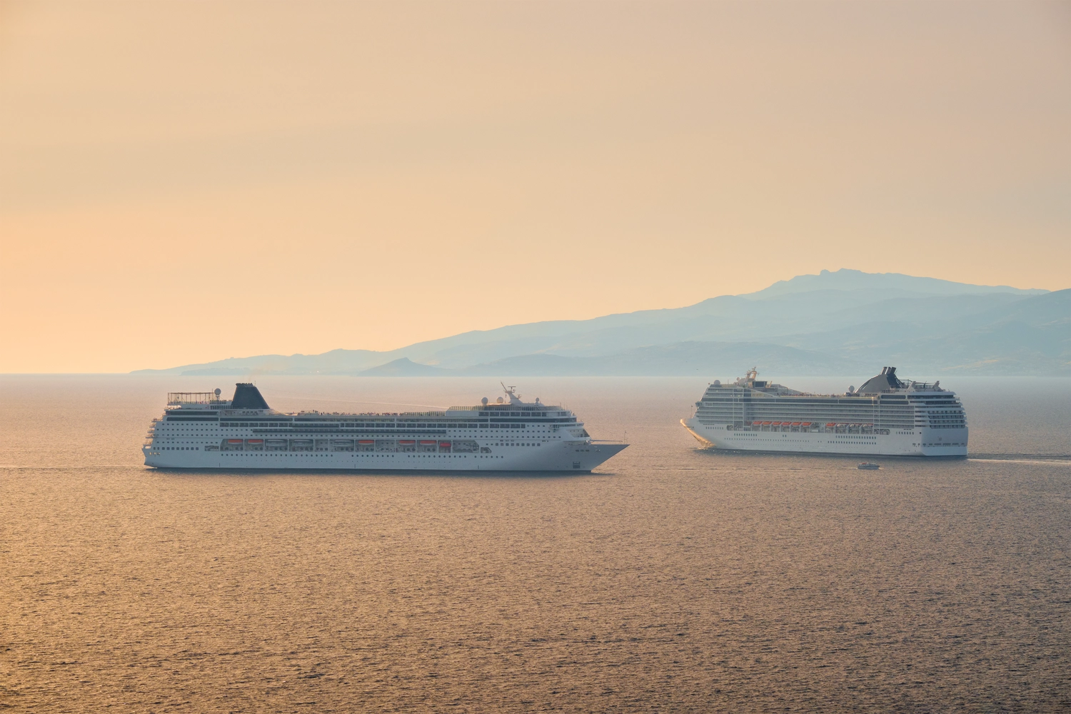 GTS - Reiseservice - Zwei große, weiße Kreuzfahrtschiffe, die parallel über den Ozean fahren, während ein goldener Sonnenuntergang in sanftem Dunst pulsiert.