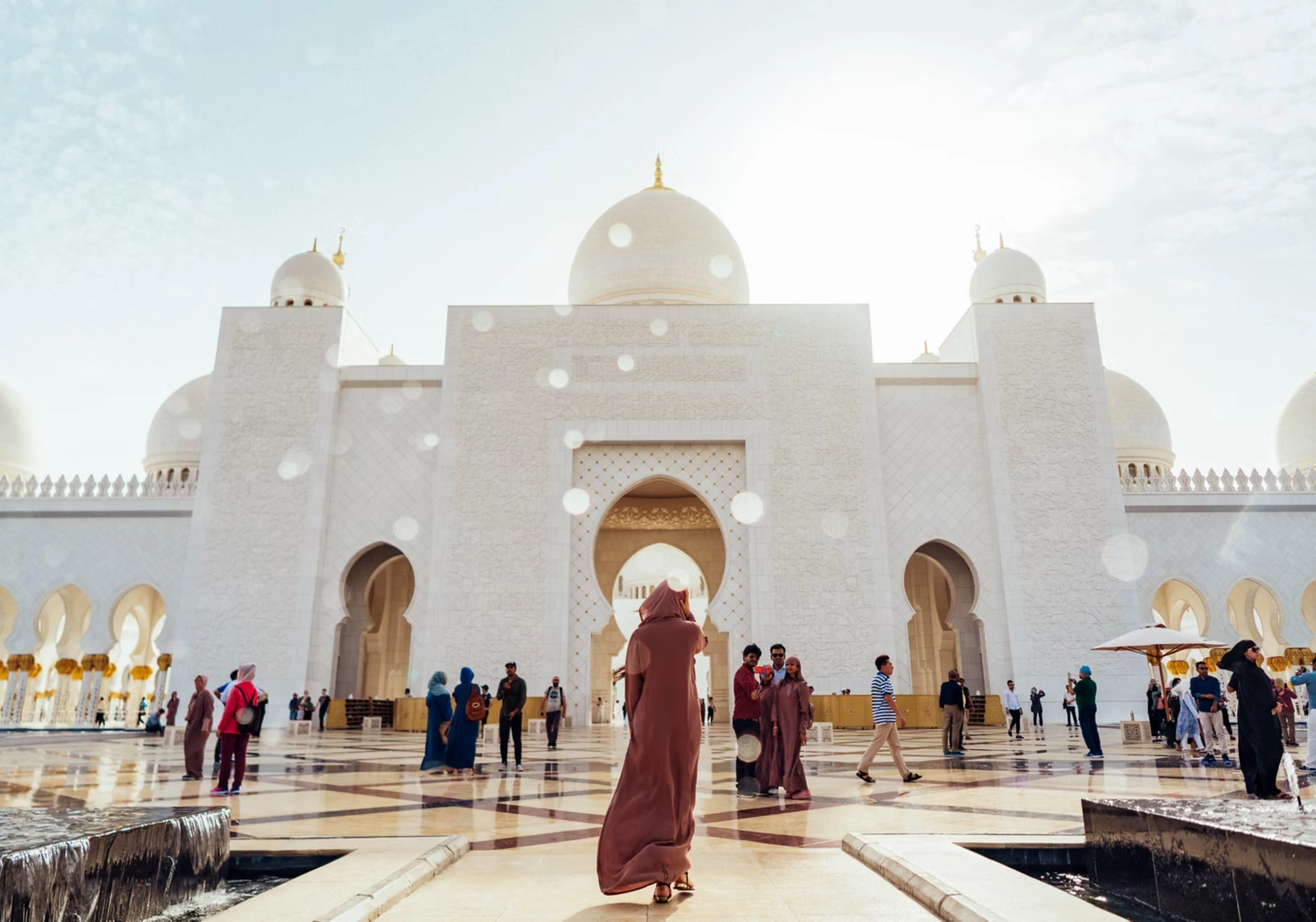 GTS - Reiseservice - Besucher erkunden den prächtigen Innenhof einer massiven Moschee aus weißem Marmor im hellen Sonnenlicht.
