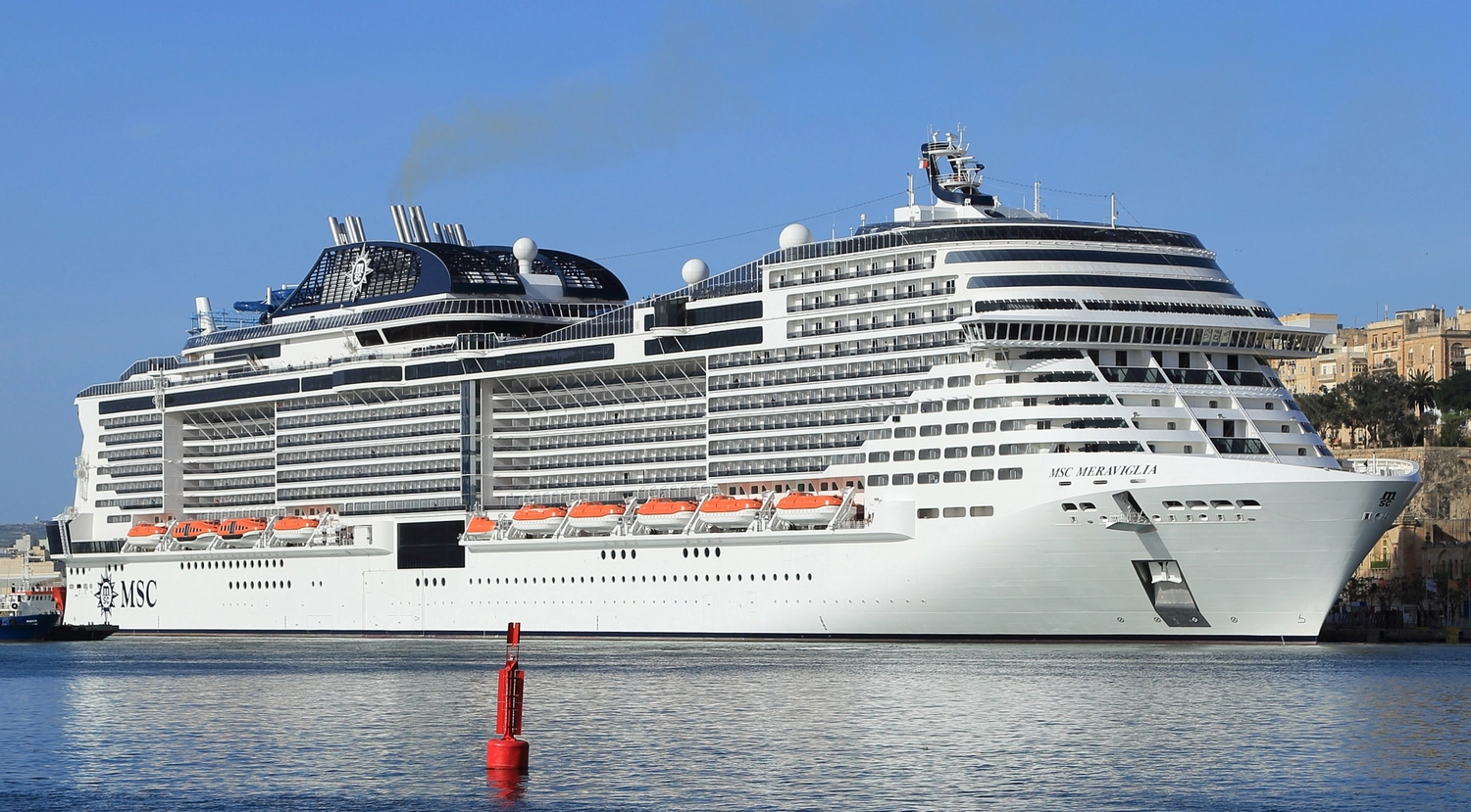 GTS - Reiseservice - Ein riesiges, weißes Kreuzfahrtschiff mit dem Schriftzug „MSC MERAVIGLIA“ liegt vor einer historischen Küste vor Anker.