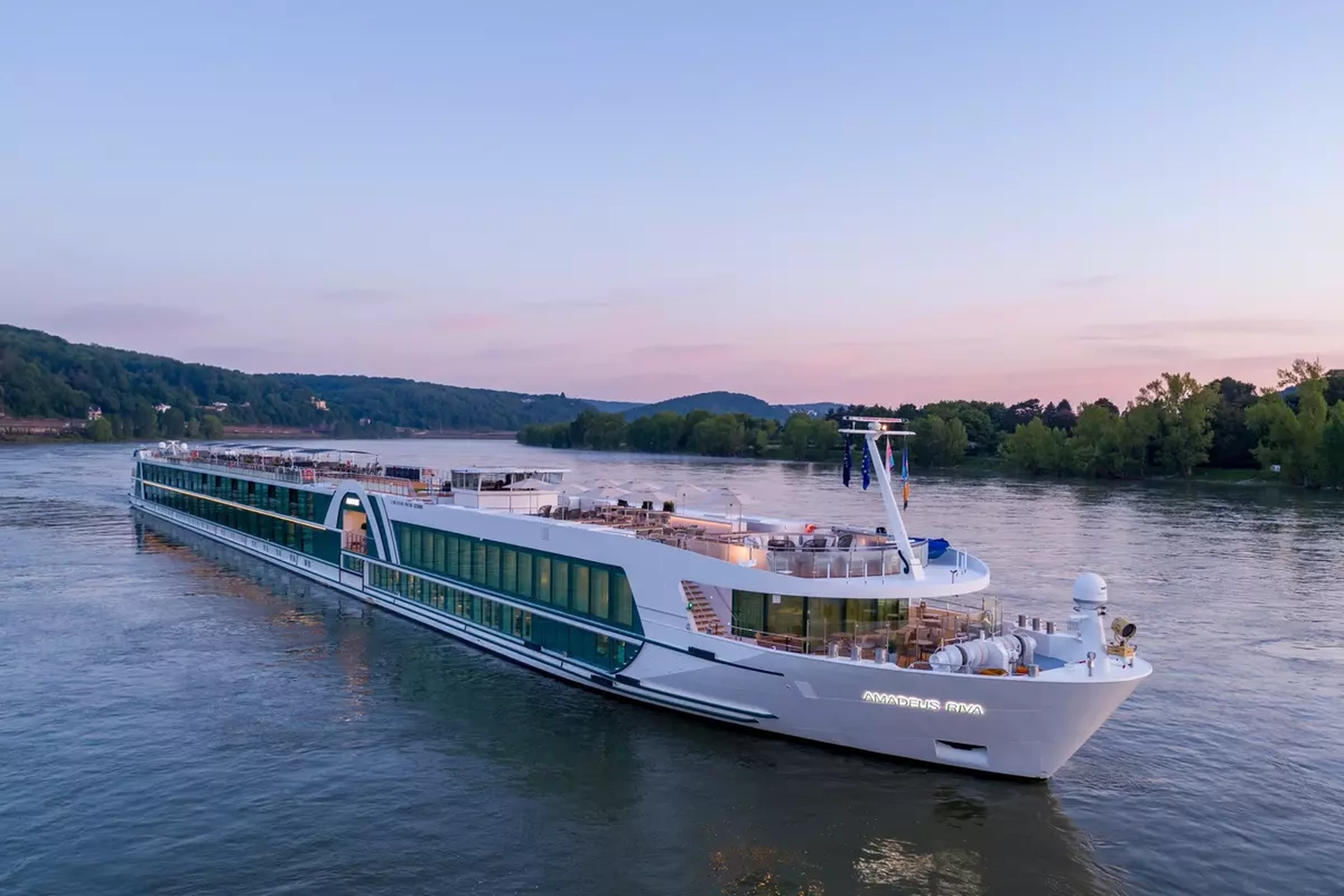 GTS - Reiseservice - Ein elegantes weiß-grünes Flusskreuzfahrtschiff namens „AMADEUS RIVA“, das in der Dämmerung auf einem ruhigen Fluss fährt.