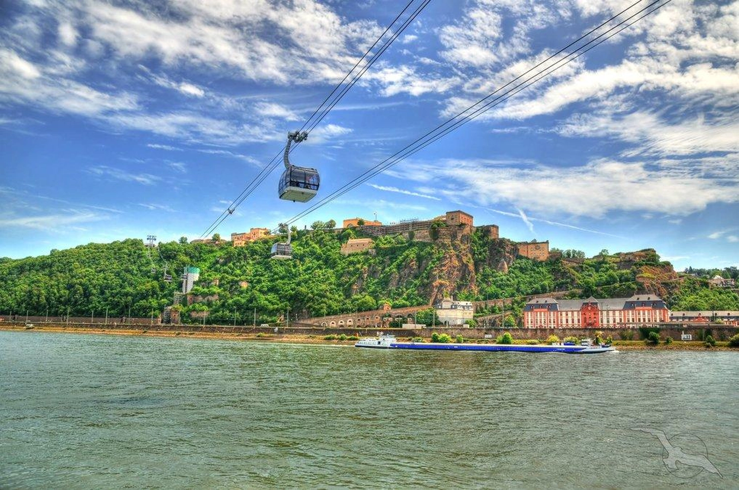 GTS - Reiseservice - Seilbahnen führen über einen breiten Fluss zu einem steilen Hang, der von steinernen Festungsmauern gesäumt ist.